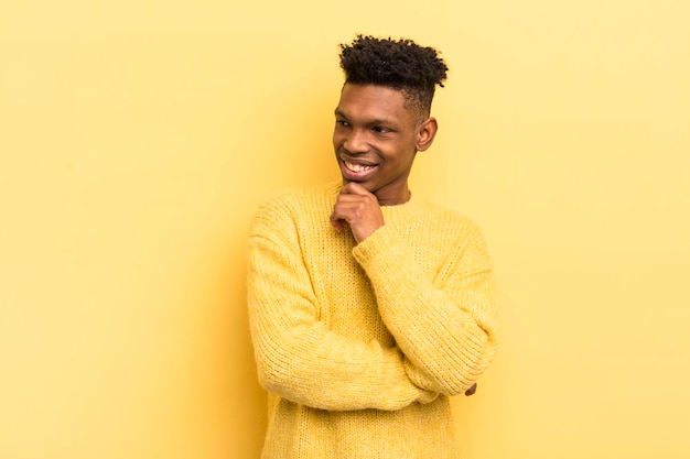 Black afro young man smiling with a happy confident expression with hand on chin wondering and looking to the side