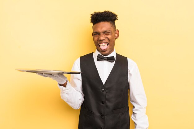 Black afro young man with cheerful and rebellious attitude joking and sticking tongue out waiter con