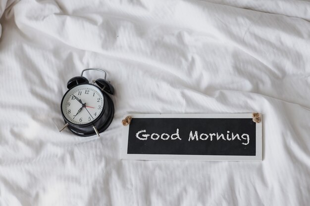 Black alarm clock on the bed with good morning sign board