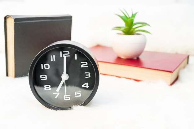 Black alarm clock and book stacked on table