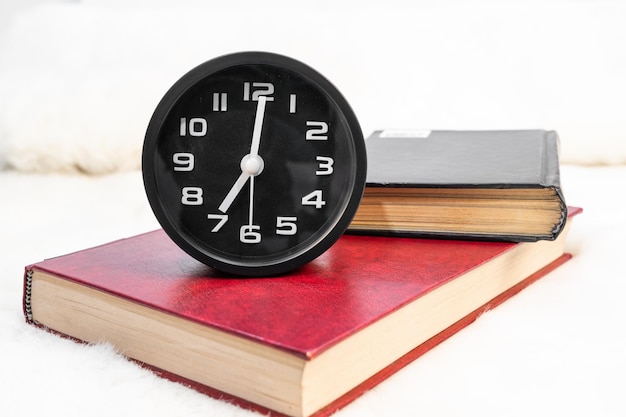 Photo black alarm clock and book stacked on table