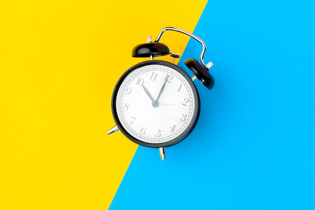 Black alarm clock on color block yellow and blue 