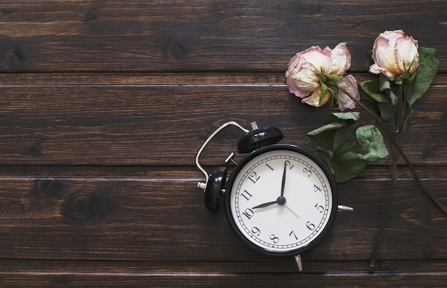 Black Alarm clock on dark wooden table with two dried roses