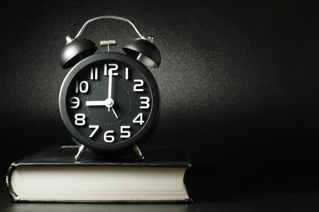 A black alarm clock placed on a thick book.