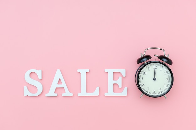 Black alarm clock and text Sale from white volume letters on pink