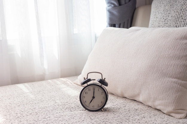 Black alarm clock on white bed in living room.