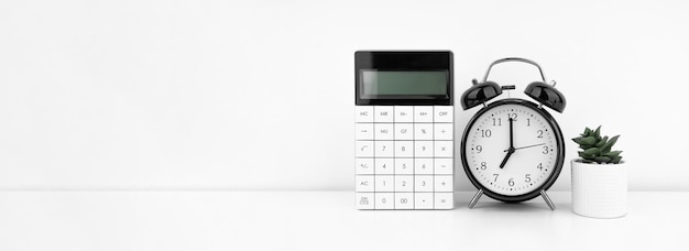 Black alarm clock with calculator against a white wall Financial concept