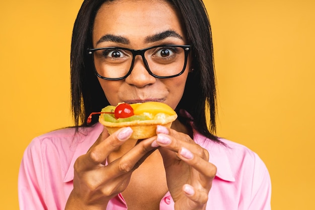 Black american african happy woman eating cake dessert isolated
over yellow background eating cupcake diet unhealthy food
concept