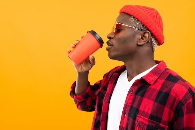Black american man in checkered red shirt drinks sideways coffee on yellow with space