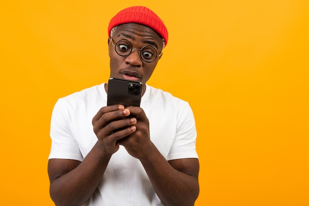 Черный американский мужчина смотрит удивленно по телефону на желтом