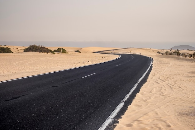모래 언덕을 건너는 사막 한가운데 검은 아스팔트 도로