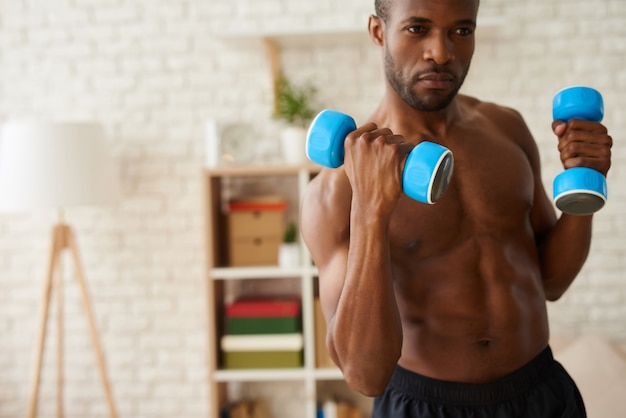 Black athlete pumping up muscles by dumbbells.
