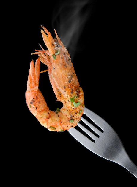 On a black backdrop, grilled shrimp with a barbecue flavor and seasonings in a spoon fork.