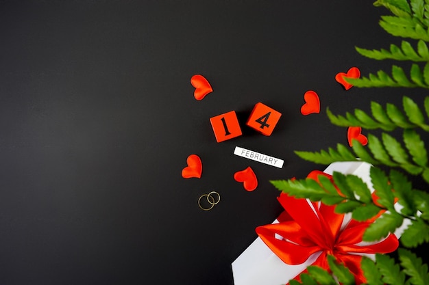 На черном фоне подарок на День святого Валентина, обручальные кольца и надпись 14 февраля.