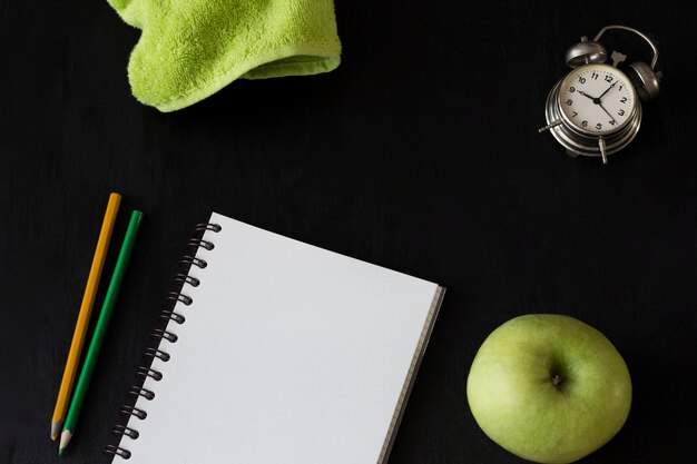 on a black background items for school: a rag, a notebook, pencils, an apple, an alarm clock 