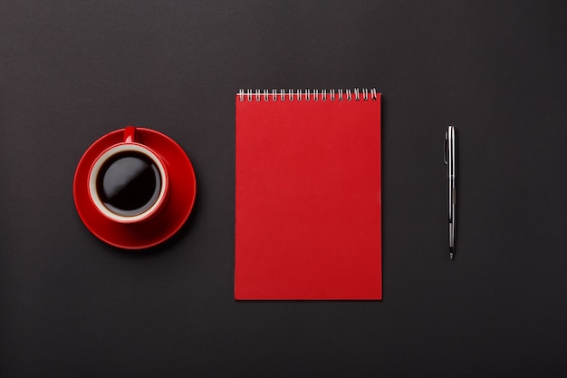 Desktop rosso dello spazio in bianco della maniglia del taccuino della tazza di caffè del fondo nero