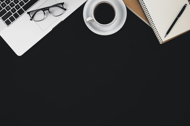 Black background with laptop notepads coffee cup and glasses