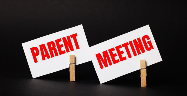 On a black background on wooden clothespins, two white blank cards with the text PARENT MEETING