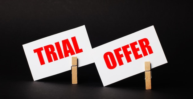 On a black background on wooden clothespins, two white blank cards with the text TRIAL OFFER.