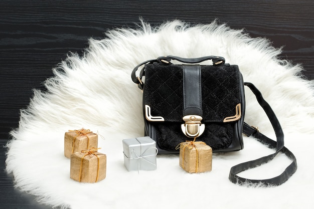 Черная сумка и подарочная коробка на белом меху. Модная концепция. Праздничный шоппинг