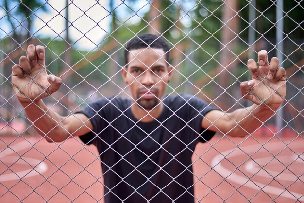 Black basketball player holding the chain link fence with hands