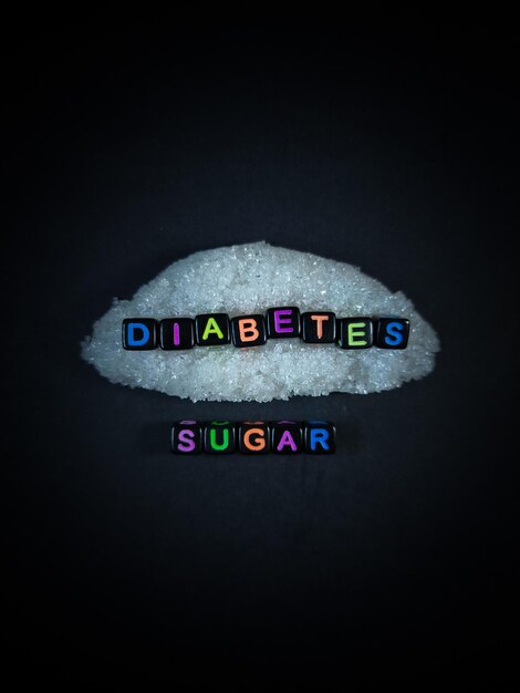 Black bead with color letter in word DIABETES LESS SUGAR with sugar and black backgroundTop view