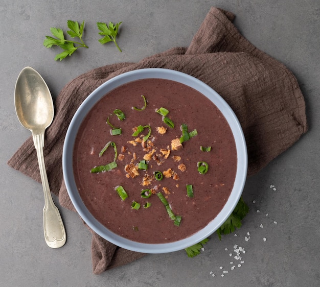 Black bean soup in a bowl with seasoning over stone background