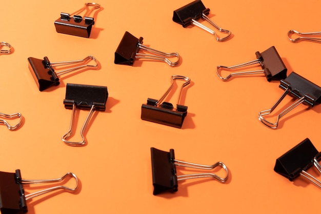 Black binder clips on orange background flat lay space for text