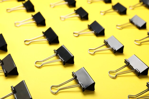 Black binder clips on yellow background Stationery items