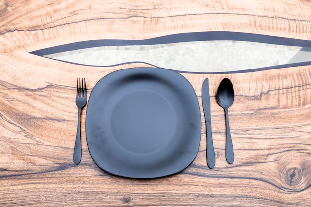 Черная черная вилка, нож, ложка и черная тарелка на деревянном столе