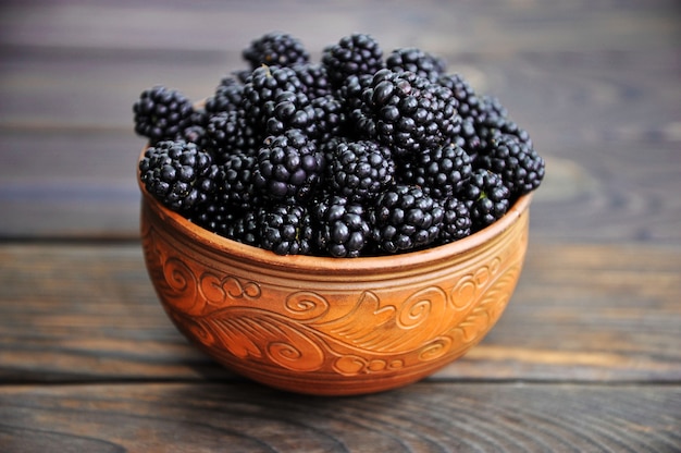 black blackberries in a pottery on a wooden table View from above