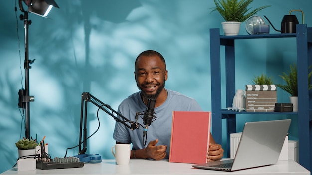 Black blogger holding book to review product on camera for vlog. African american influencer reviewing notebook for social media channel. POV of vlogger doing recommendation on video