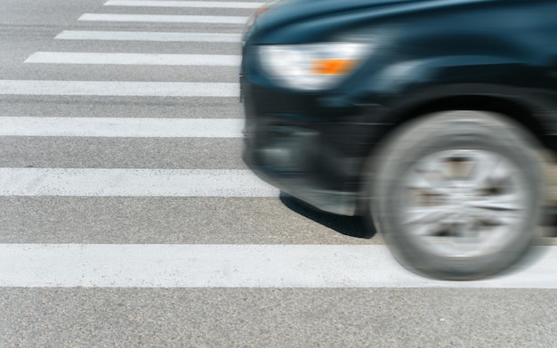 Automobile nera sfocata che guida veloce sulle strisce pedonali all'aperto vista laterale del primo piano messa a fuoco selettiva sui segni bianchi dell'attraversamento pedonale