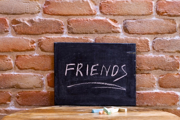 Foto tavola nera con la parola amici annegati a mano su un tavolo di legno sullo sfondo di una parete di mattoni concetto di amicizia