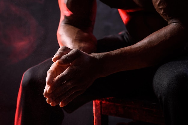 Black bodybuilder uses hand talcum powder A man sits on a black background with red smoke