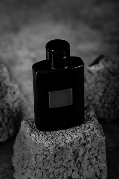 Черная бутылка туалетной воды среди серых камней Мужской аромат