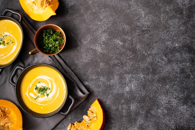 Black bowl with pumpkin autumn soup. Vegan delicious, creamy soup with coconut milk. Top view. Dark background.