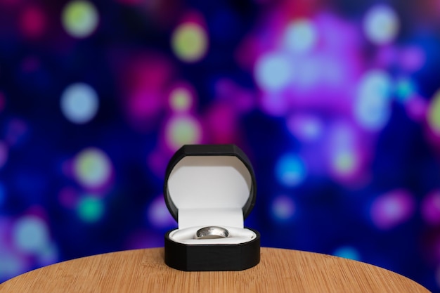Foto una scatola nera con anello con coperchio bianco si trova su un tavolo di legno con bokeh colorato sullo sfondo