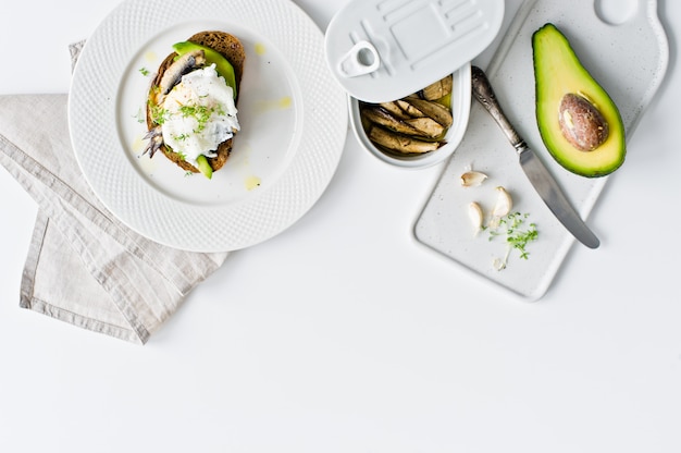 Black bread sandwich with avocado, poached egg and sprats. 