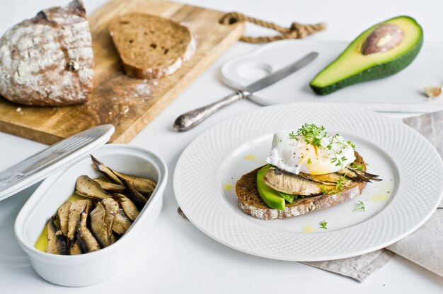 Black bread sandwich with avocado, poached egg and sprats.