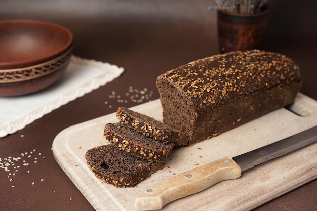 Black Bread with cereals Sliced on a wooden cutting board against a brown background