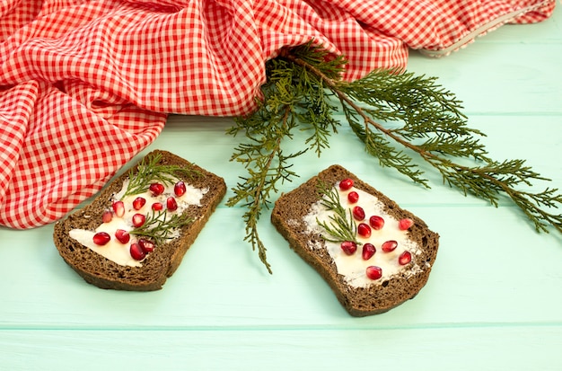 Black bread with grenades berries on turquoise wooden background. Christmas food, Christmas decorations with lemon, juniper, branch, red berries