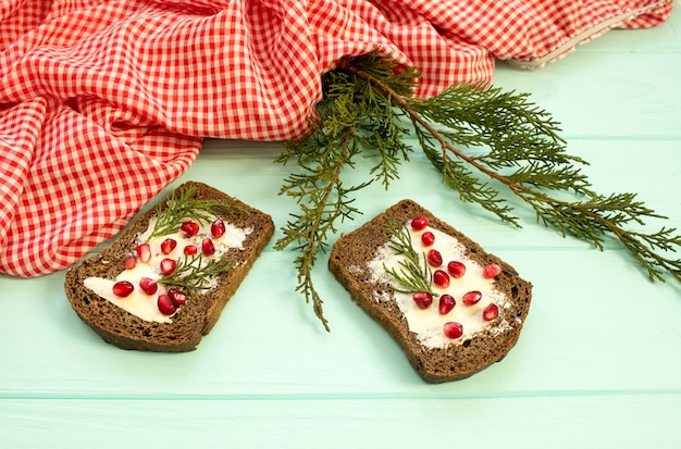 Pane nero con bacche di granate sul fondo in legno turchese. alimento di natale, decorazioni natalizie con limone, ginepro, ramo, bacche rosse