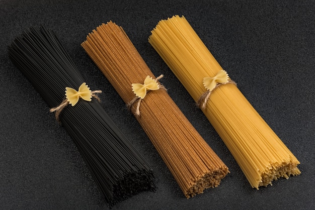 Black, brown and yellow dry spaghetti on gray table. Italian ingredients