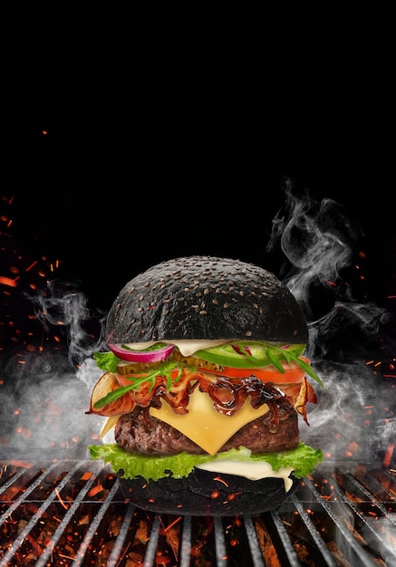 Black burger roasted on barbecue grill with flaming fire sparks and smoke against black background b...