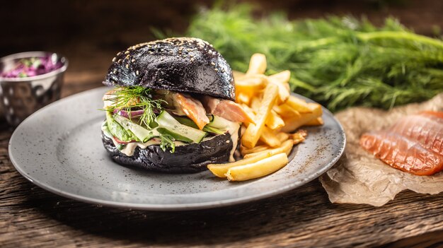 Salmone ripieno di hamburger nero, avocado e insalata di cetrioli con patatine fritte.