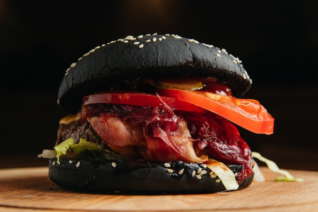 Black burger with bacon on wooden board