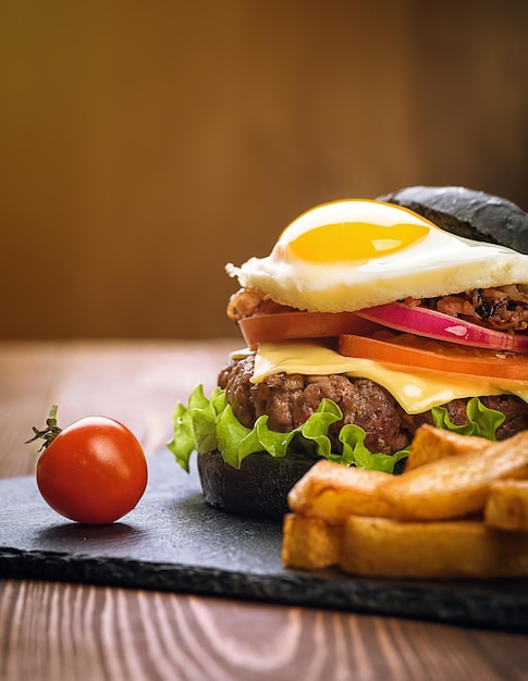 Foto burger nero con un uovo su un piatto di pietra pomodori di ciliegio patate fritte