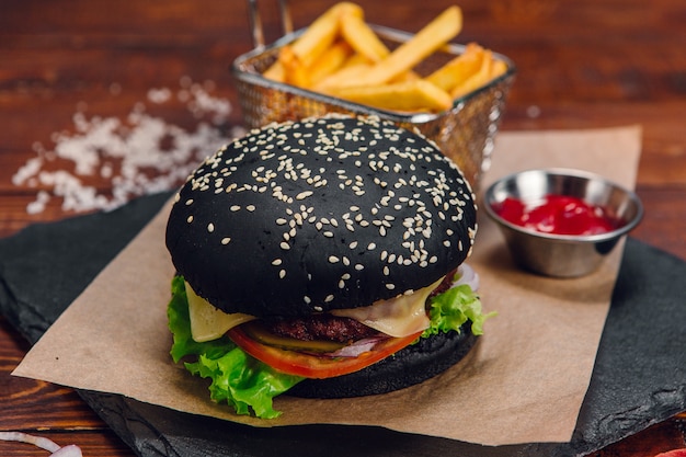 Black burger with fries and ketchup on a table in a restaurant