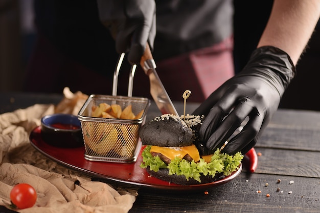 Black burger with fries and sauce. In a red plate on a wooden table